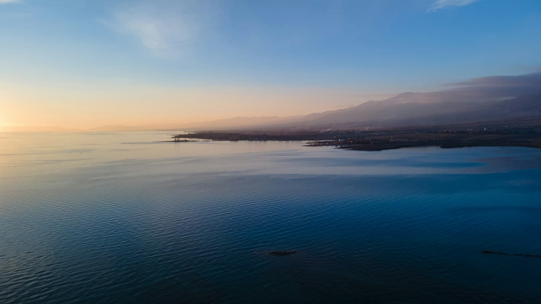 Wide alpine water at dusk with a distant shoreline and mountain haze, recalling Issyk-Kul