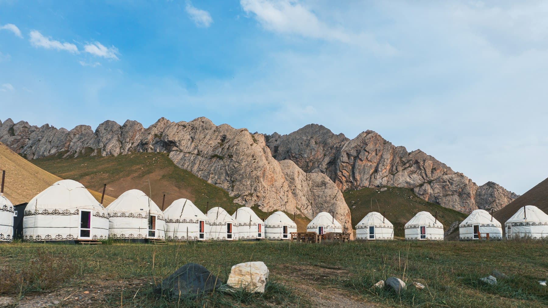 White yurts lined across an alpine meadow with mountains behind